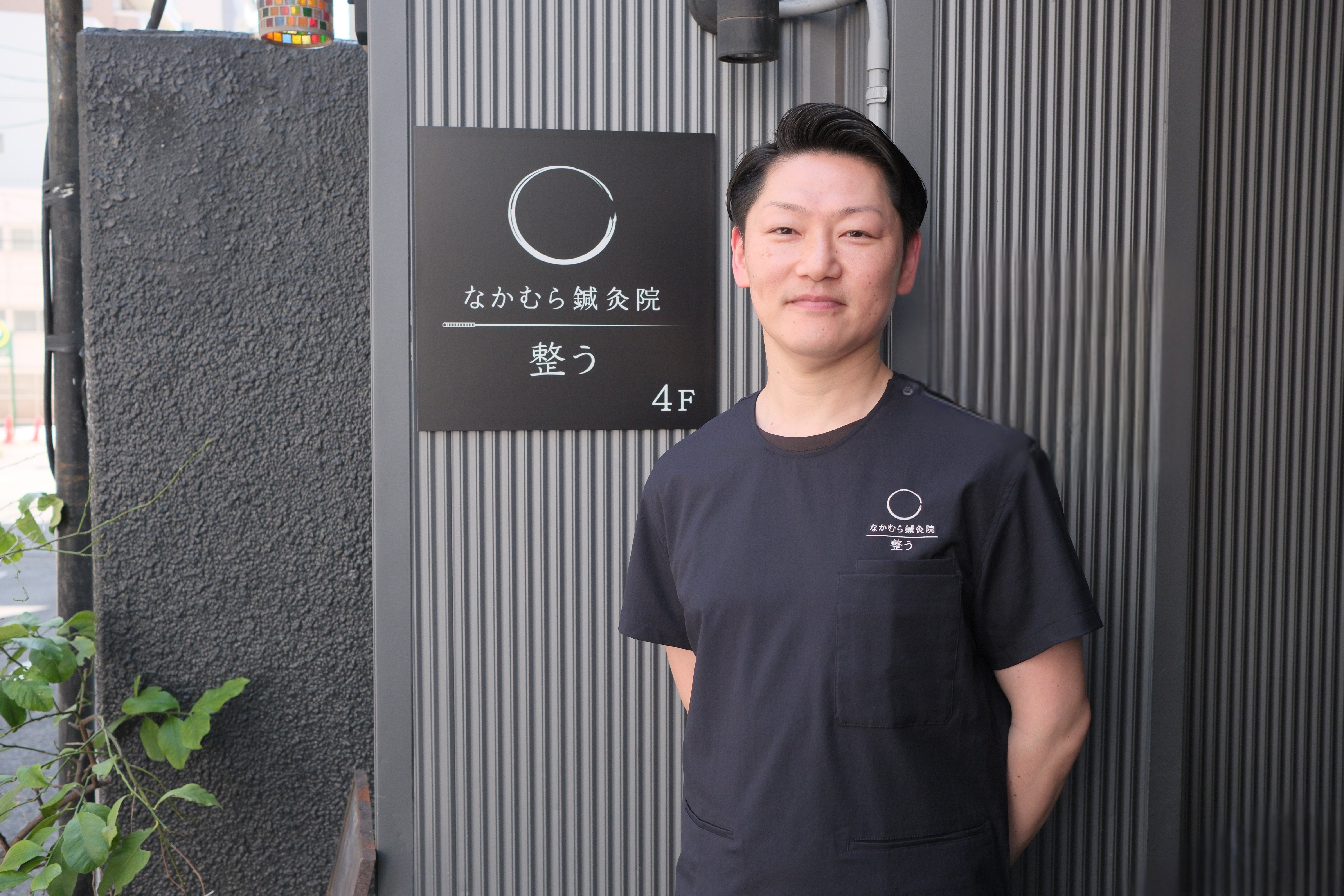 Man standing in front of Japanese acupuncture clinic entrance sign on building