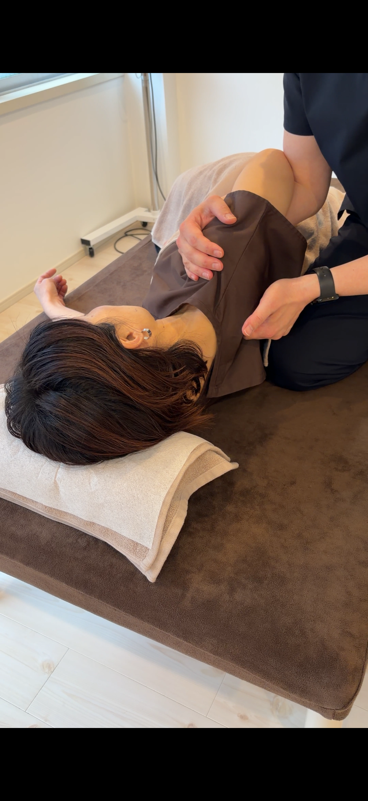 Physiotherapist performing knee examination on patient lying on treatment table