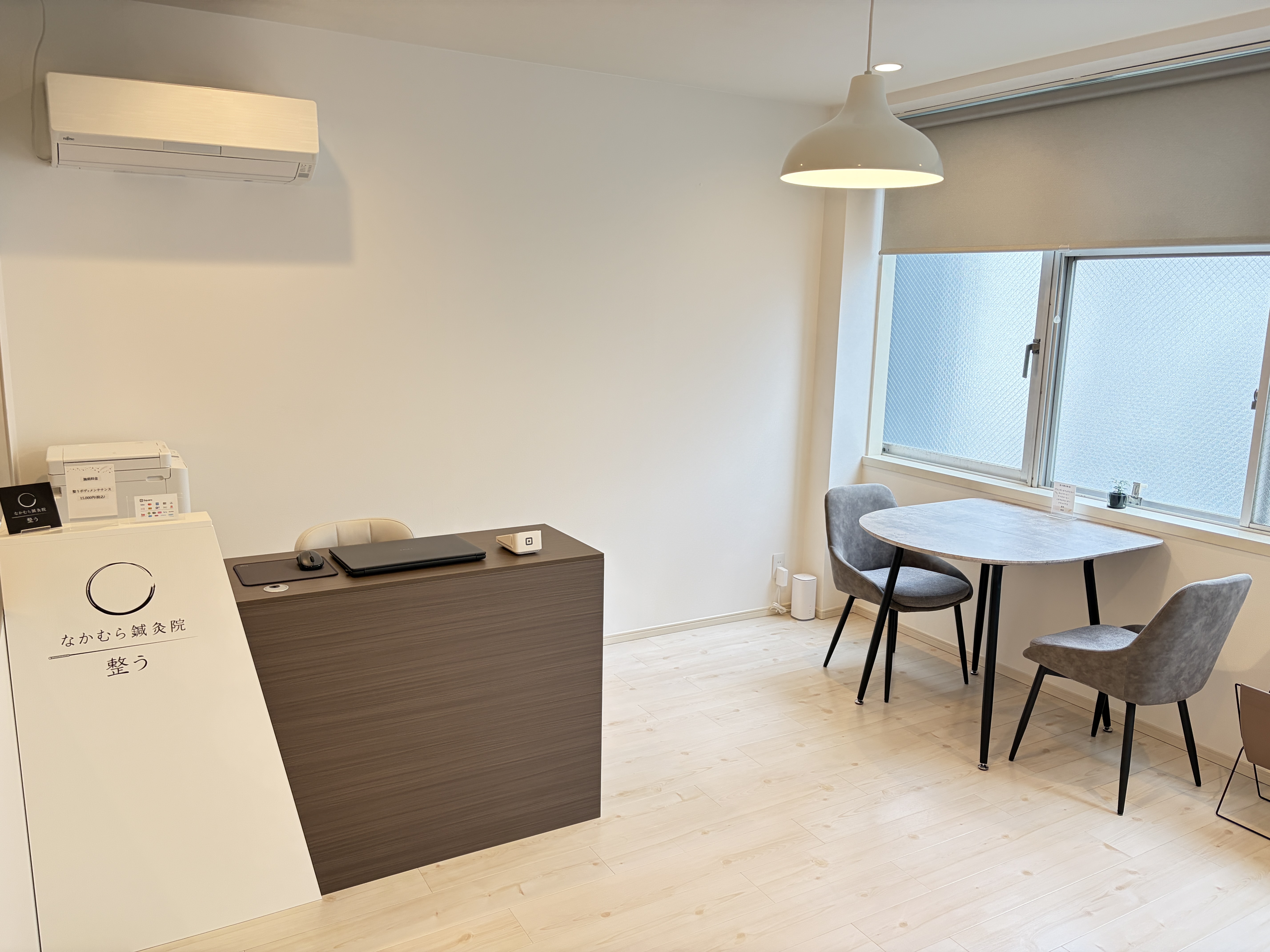 Modern acupuncture clinic interior with reception desk, waiting area table, and chairs by windows